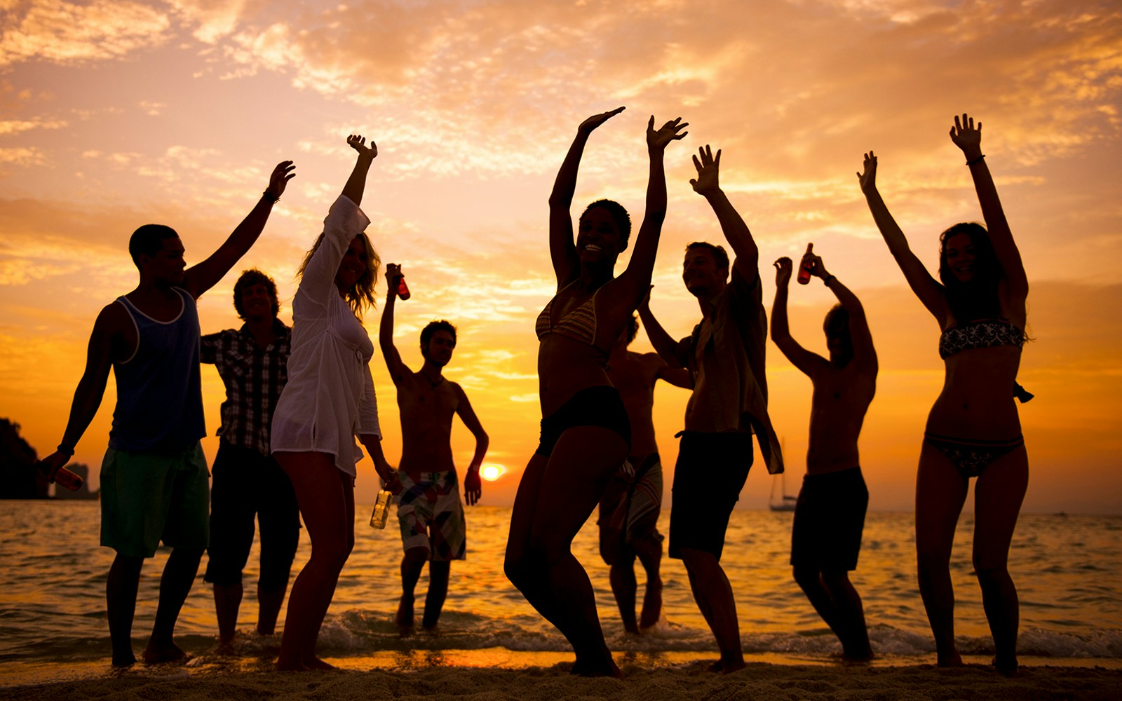 People dancing on a beach at sunset with the ocean in the background.