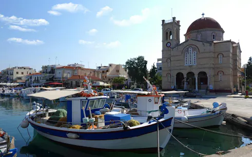 Fishing boats docked at Aegina harbor with a church in the background, Greece.