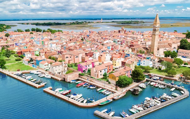 Aerial view of colorful Burano island with boats and canal during helicopter tour over the lagoon.