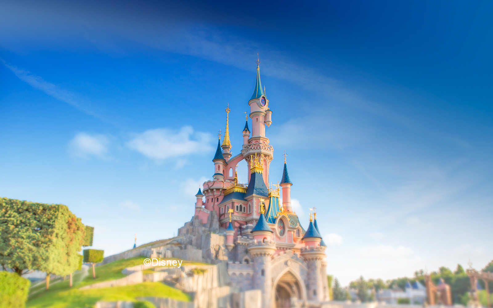 Sleeping Beauty Castle at Disneyland Paris with vibrant blue turrets and lush greenery.