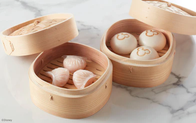 Steamed dumplings and buns with Mickey Mouse logo in bamboo baskets at Disneyland Hong Kong.