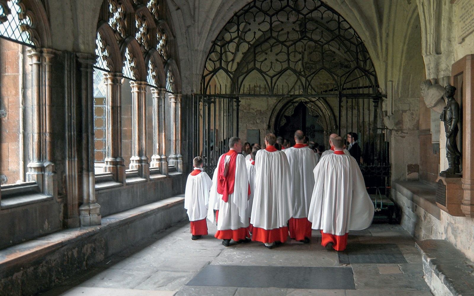 Choristers in red and white robes walking through Westminster Abbey cloisters.