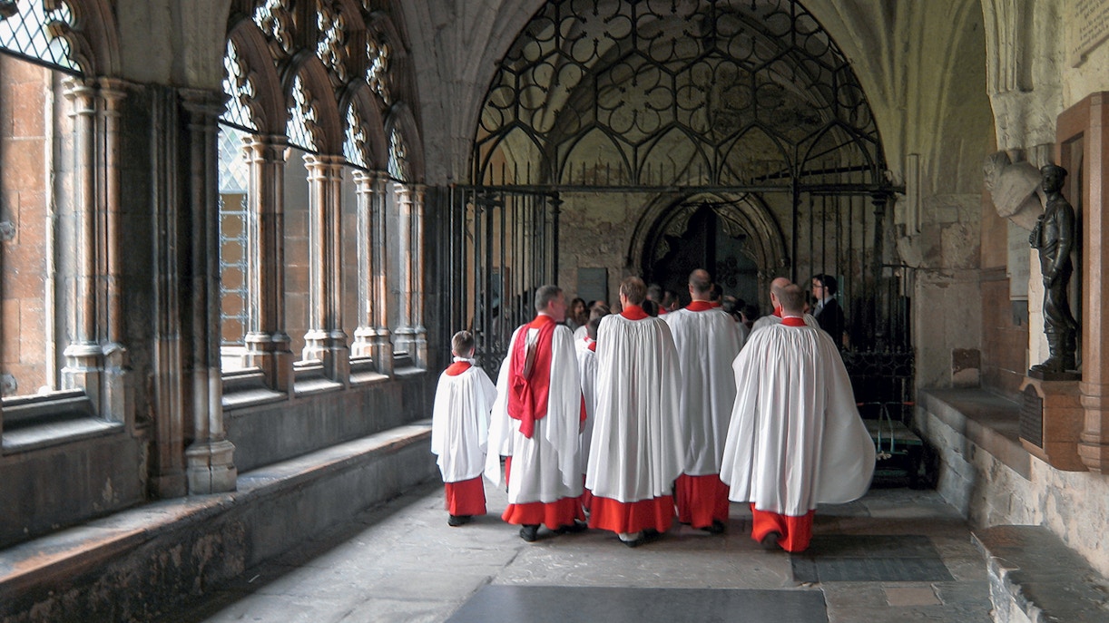 Choristers in red and white robes walking through Westminster Abbey cloisters.