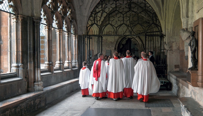 Choristers in red and white robes walking through Westminster Abbey cloisters.