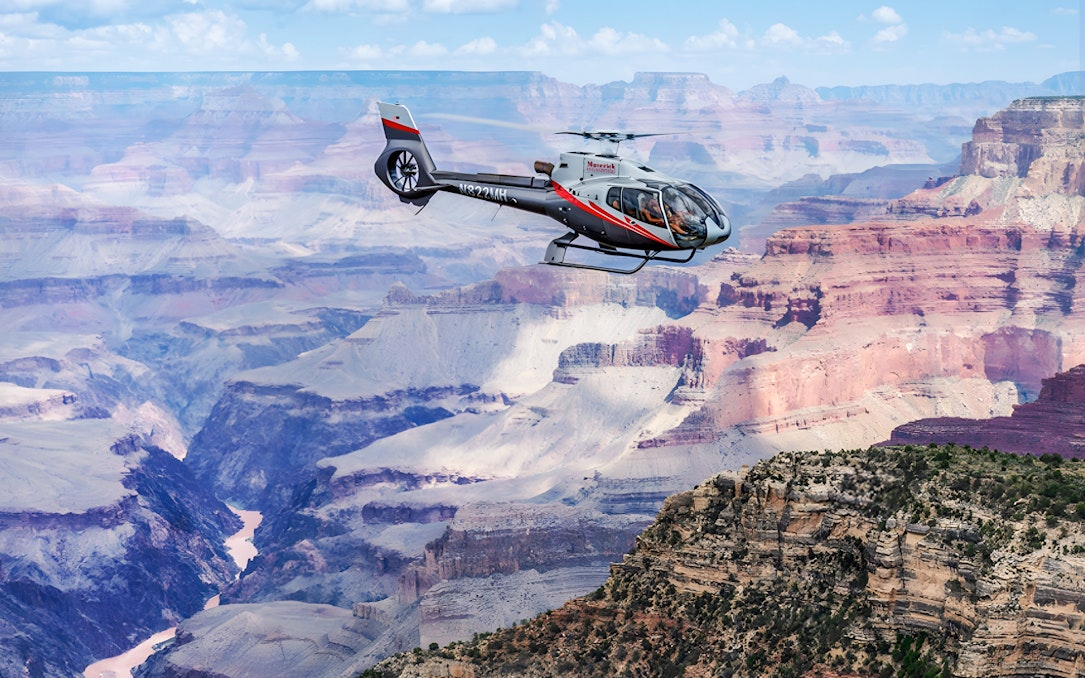 Helicopter flying over the Grand Canyon with colorful rock formations below.
