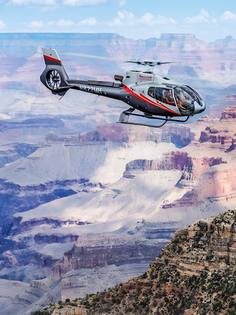 Helicopter flying over the Grand Canyon with colorful rock formations below.