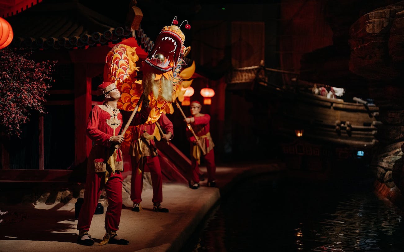 Performers in traditional attire with dragon puppet at World of Discoveries Interactive Digital Exhibition.