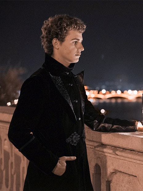 Person in dark attire holding lantern on Buda Castle tour, Budapest, with city lights in background.