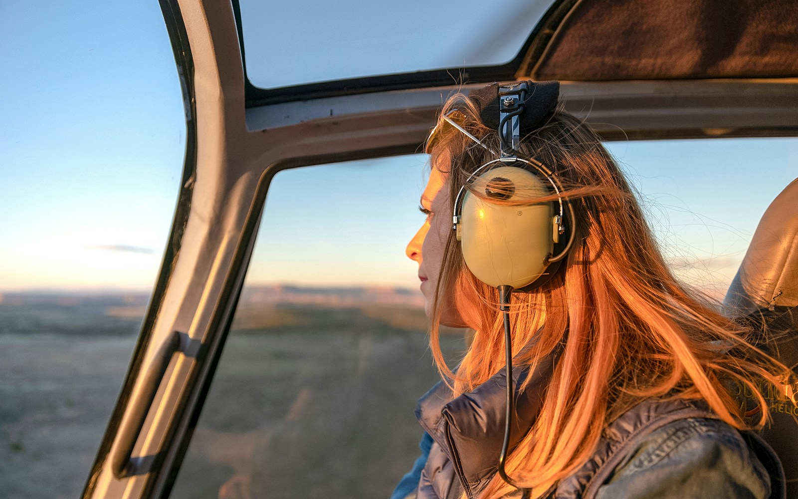 Girl wearing headphones in helicopter over Grand Canyon at sunset.