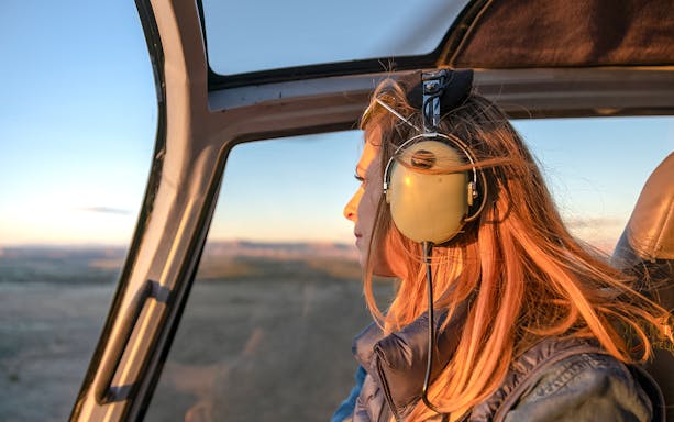 Girl wearing headphones in helicopter over Grand Canyon at sunset.