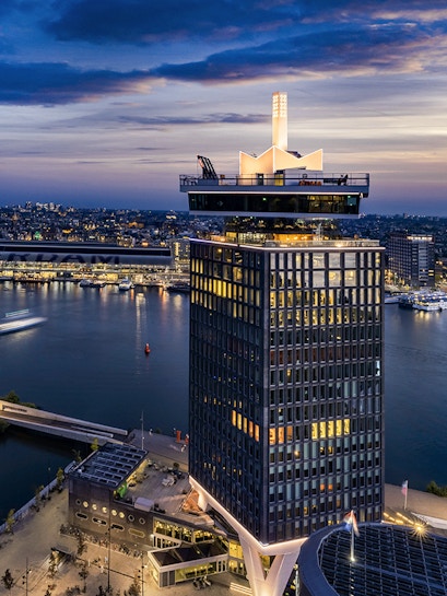 A'DAM Lookout tower overlooking Amsterdam at dusk with city lights and river.