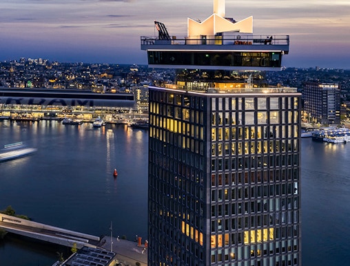 A'DAM Lookout tower overlooking Amsterdam at dusk with city lights and river.