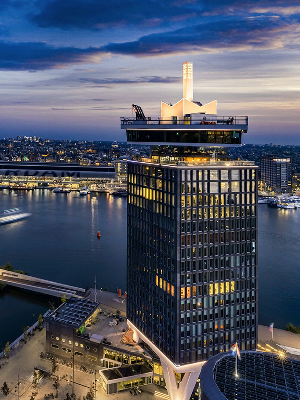 A'DAM Lookout tower overlooking Amsterdam at dusk with city lights and river.