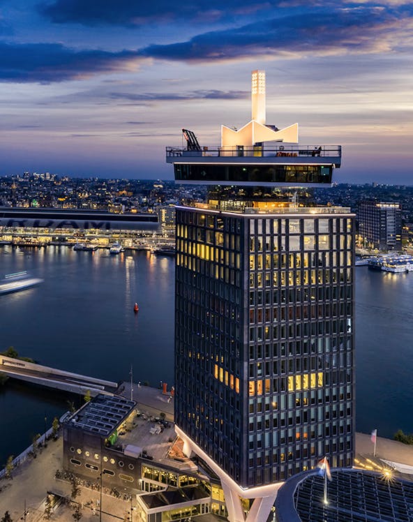 A'DAM Lookout tower overlooking Amsterdam at dusk with city lights and river.