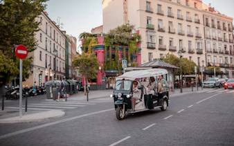 Tourists on an electric tuk-tuk tour in a vibrant Madrid street.