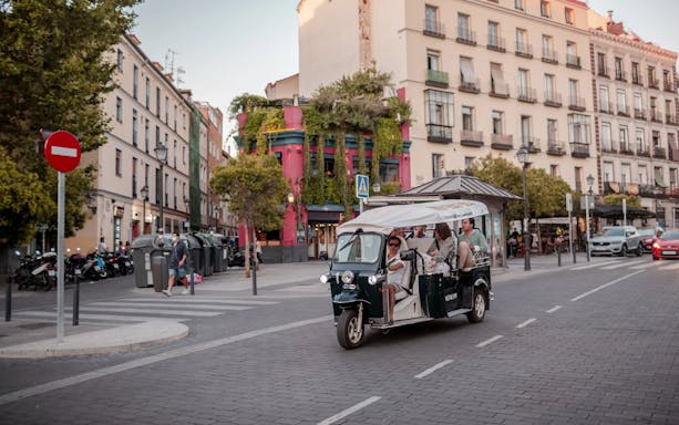 Tourists on an electric tuk-tuk tour in a vibrant Madrid street.
