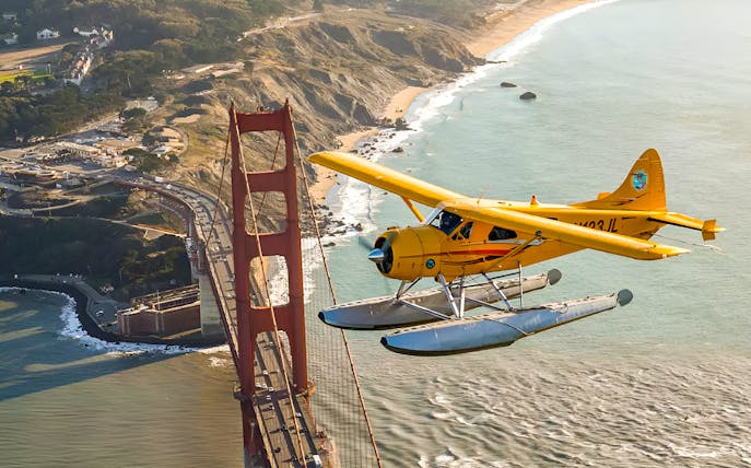 Seaplane flying over Golden Gate Bridge, San Francisco coast in view.