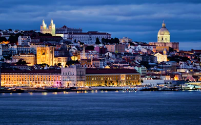 Lisbon view over Tagus River with Alfama district, National Pantheon, Monastery of St. Vincent, and ferry at twilight.