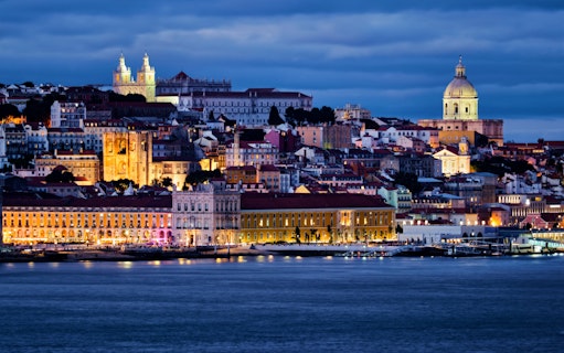 Lisbon view over Tagus River with Alfama district, National Pantheon, Monastery of St. Vincent, and ferry at twilight.