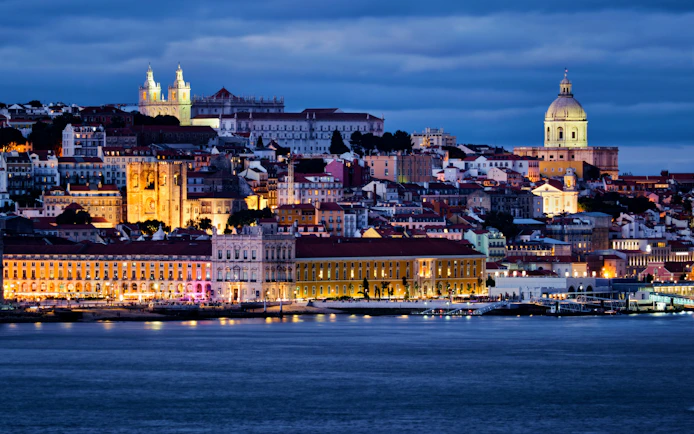 Lisbon view over Tagus River with Alfama district, National Pantheon, Monastery of St. Vincent, and ferry at twilight.