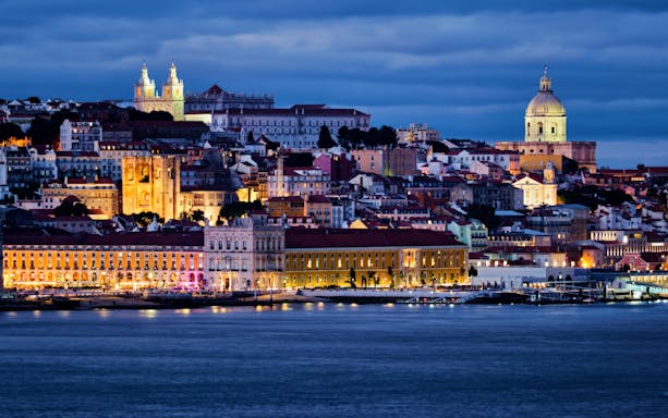 Lisbon view over Tagus River with Alfama district, National Pantheon, Monastery of St. Vincent, and ferry at twilight.