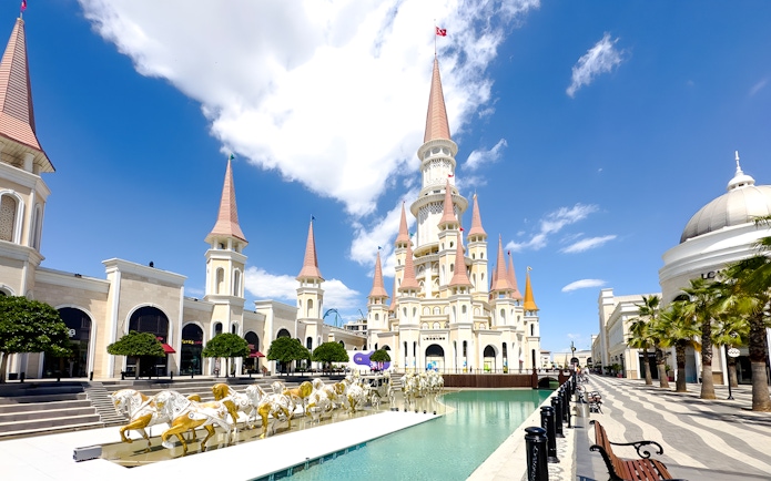 Land of Legends Themepark castle with spires and horse statues by a water feature.