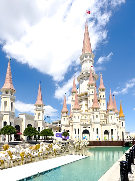 Land of Legends Themepark castle with spires and horse statues by a water feature.