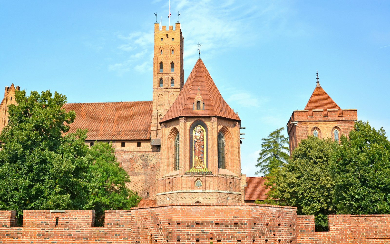 Main tower and chapel of St. Anne Malbork Castle with brick walls and trees.