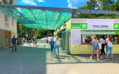 Visitors at Prague Zoo ticket office under a green canopy.