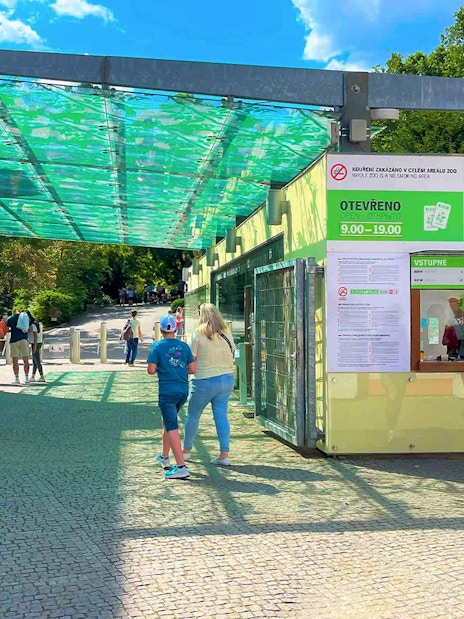 Visitors at Prague Zoo ticket office under a green canopy.