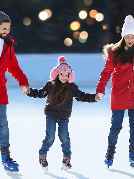 Family ice skating together at an outdoor rink.