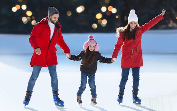 Family ice skating together at an outdoor rink.