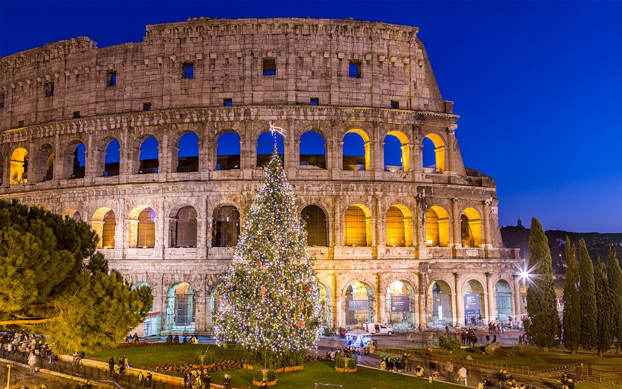 Colosseum in Rome with a decorated Christmas tree in front during evening celebration.