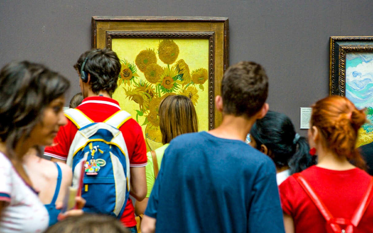 Visitors viewing Van Gogh's Sunflowers painting in a museum.