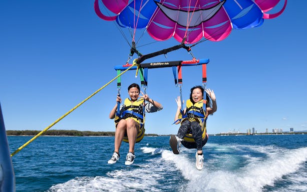 Parasailing over ocean with city skyline in background.