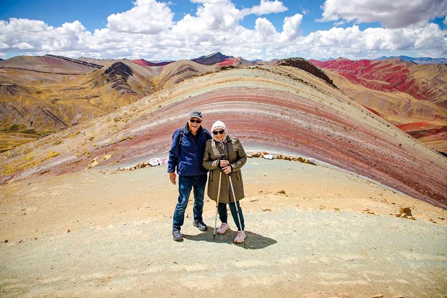 Couple standing on colorful Palcoyo Mountain with Red Valley in background, Cusco.