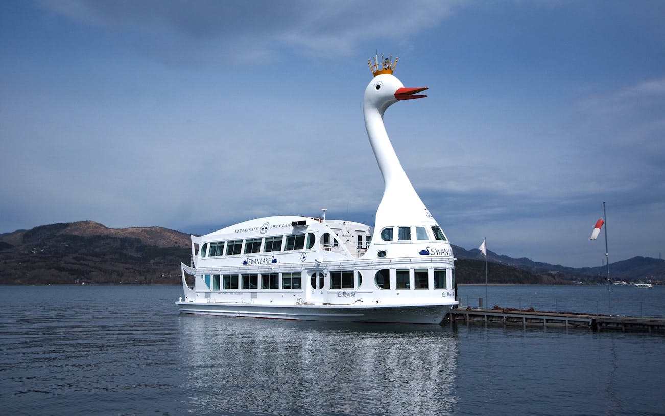 Swan-shaped cruise boat on Lake Yamanaka with mountains in the background.