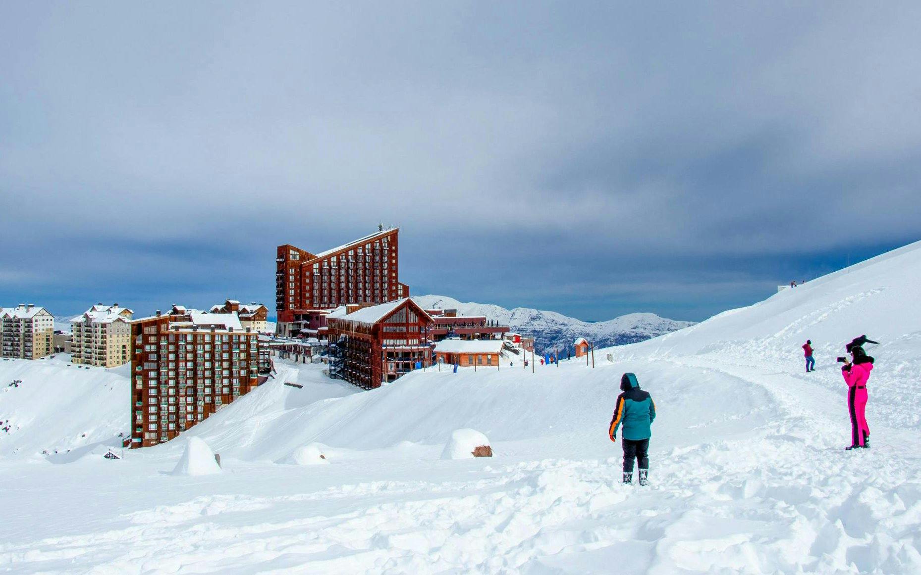 Tourists at Valle Nevado ski resort in the Andes Mountains, Chile, with snowy slopes and buildings.
