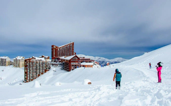 Tourists at Valle Nevado ski resort in the Andes Mountains, Chile, with snowy slopes and buildings.