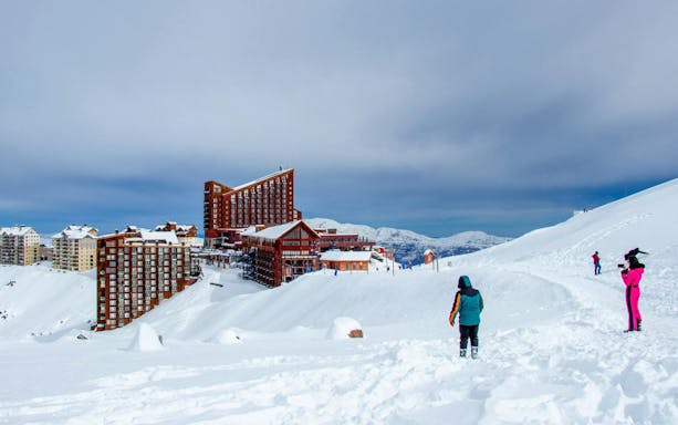 Tourists at Valle Nevado ski resort in the Andes Mountains, Chile, with snowy slopes and buildings.