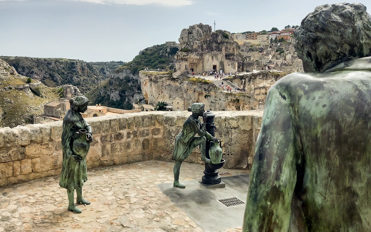 Statues overlooking Matera's ancient stone cityscape, featuring Casa Grotta.
