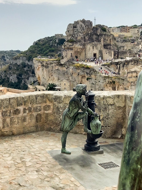 Statues overlooking Matera's ancient stone cityscape, featuring Casa Grotta.
