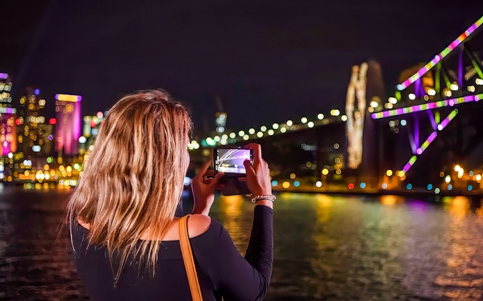 Woman photographing illuminated Sydney Harbour Bridge during Vivid Lights Cruise.
