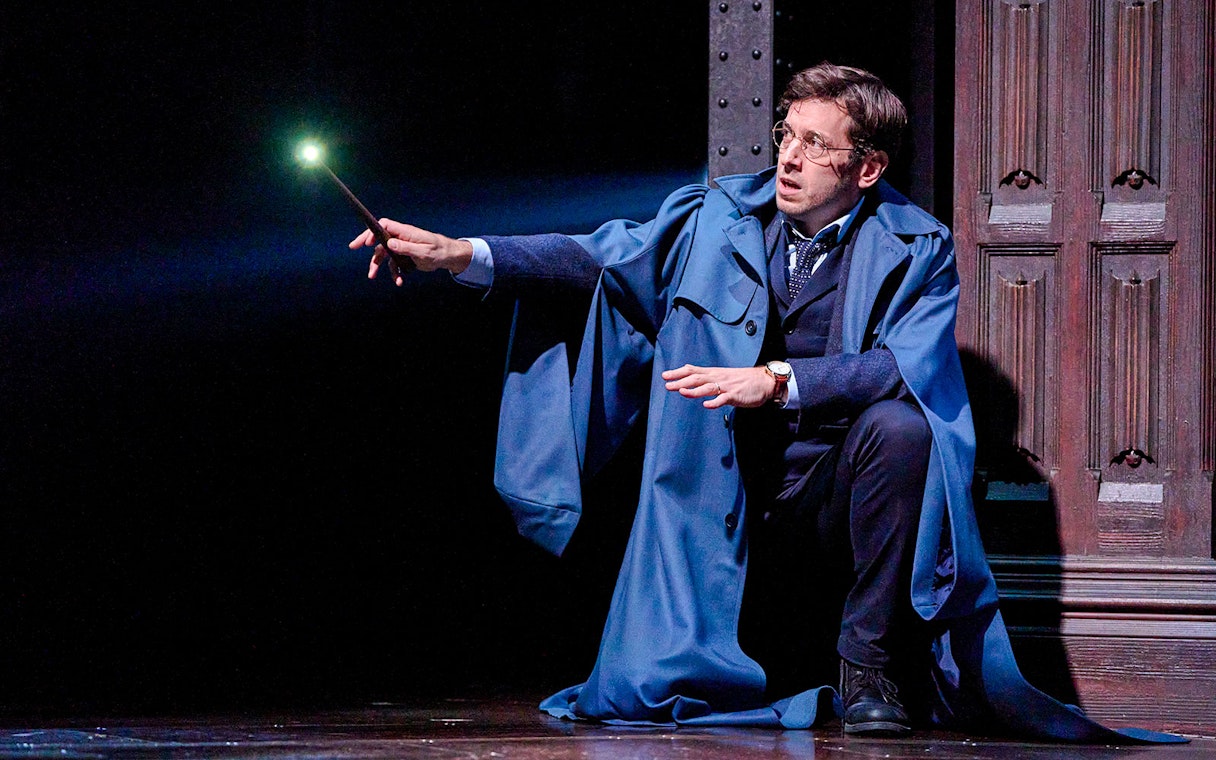 Actor holding a glowing wand in "Harry Potter and the Cursed Child" stage scene.