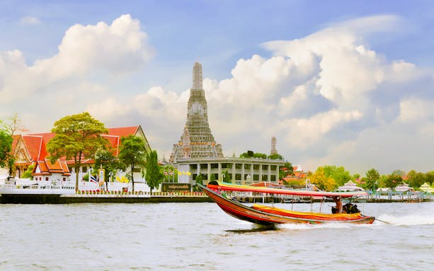 Long-tail boat on Chao Phraya River with Wat Arun in the background, Bangkok.