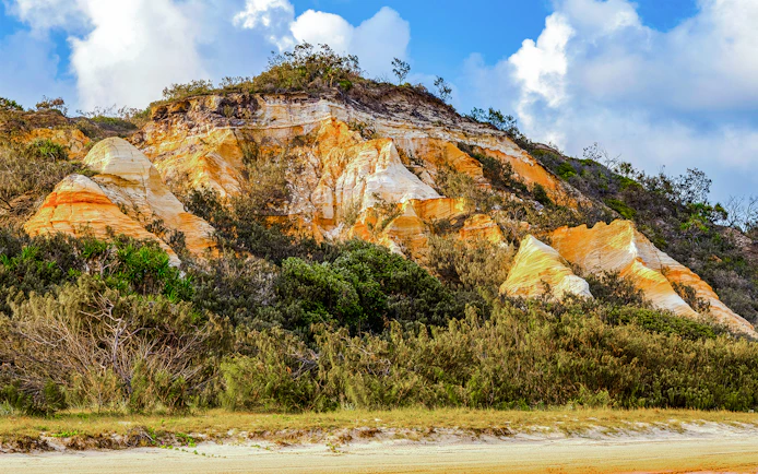 The Pinnacles' colorful sand cliffs on Fraser Island, K'gari, with lush vegetation.