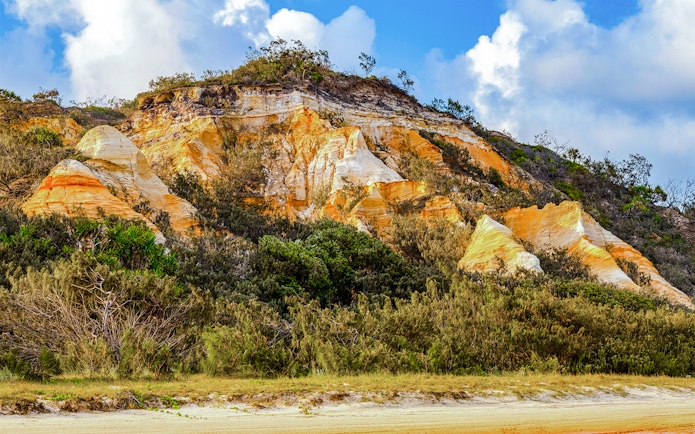 The Pinnacles' colorful sand cliffs on Fraser Island, K'gari, with lush vegetation.