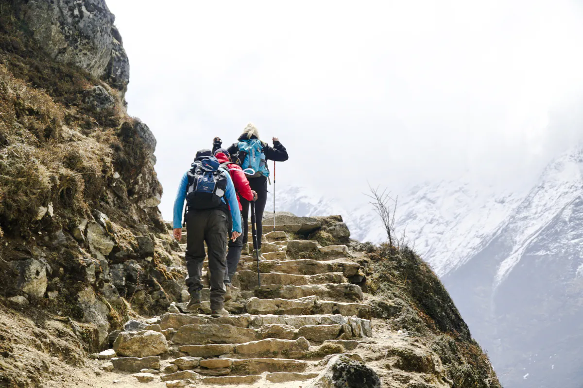 Trekkers ascending rocky steps with snowy mountains in Everest Region.