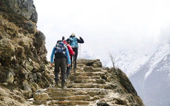 Trekkers ascending rocky steps with snowy mountains in Everest Region.