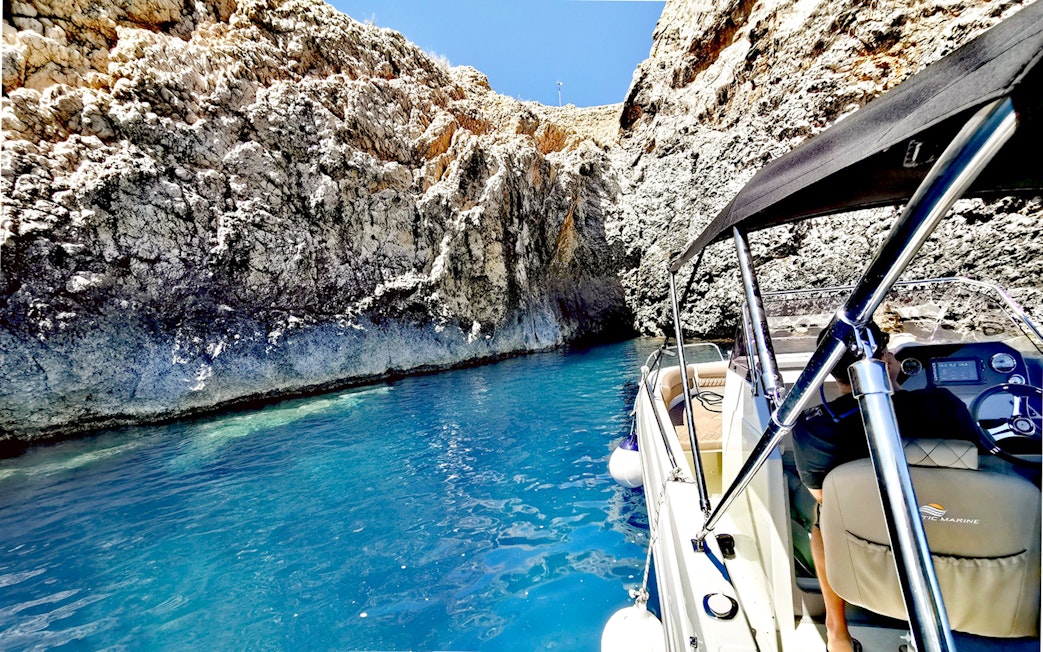 Boat entering a blue cave with rocky walls and clear water.